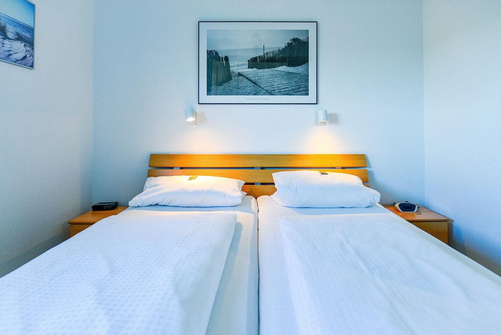 Zwei Einzelbetten mit weißen Bettwäsche, Holzkopfteil und Wandbild über dem Bett.