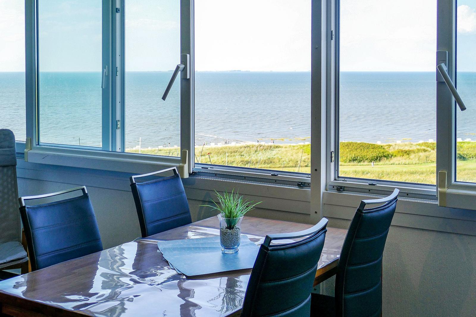 Esstisch mit Stühlen vor großem Fenster mit Meerblick.