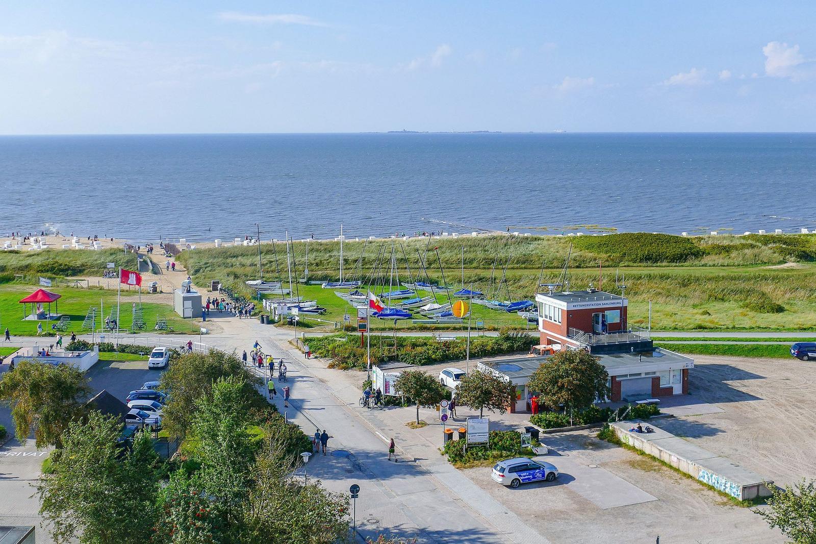 Strandufer mit Bootsanlegestelle und Rettungsstation. Menschen spazieren entlang des Meeres.