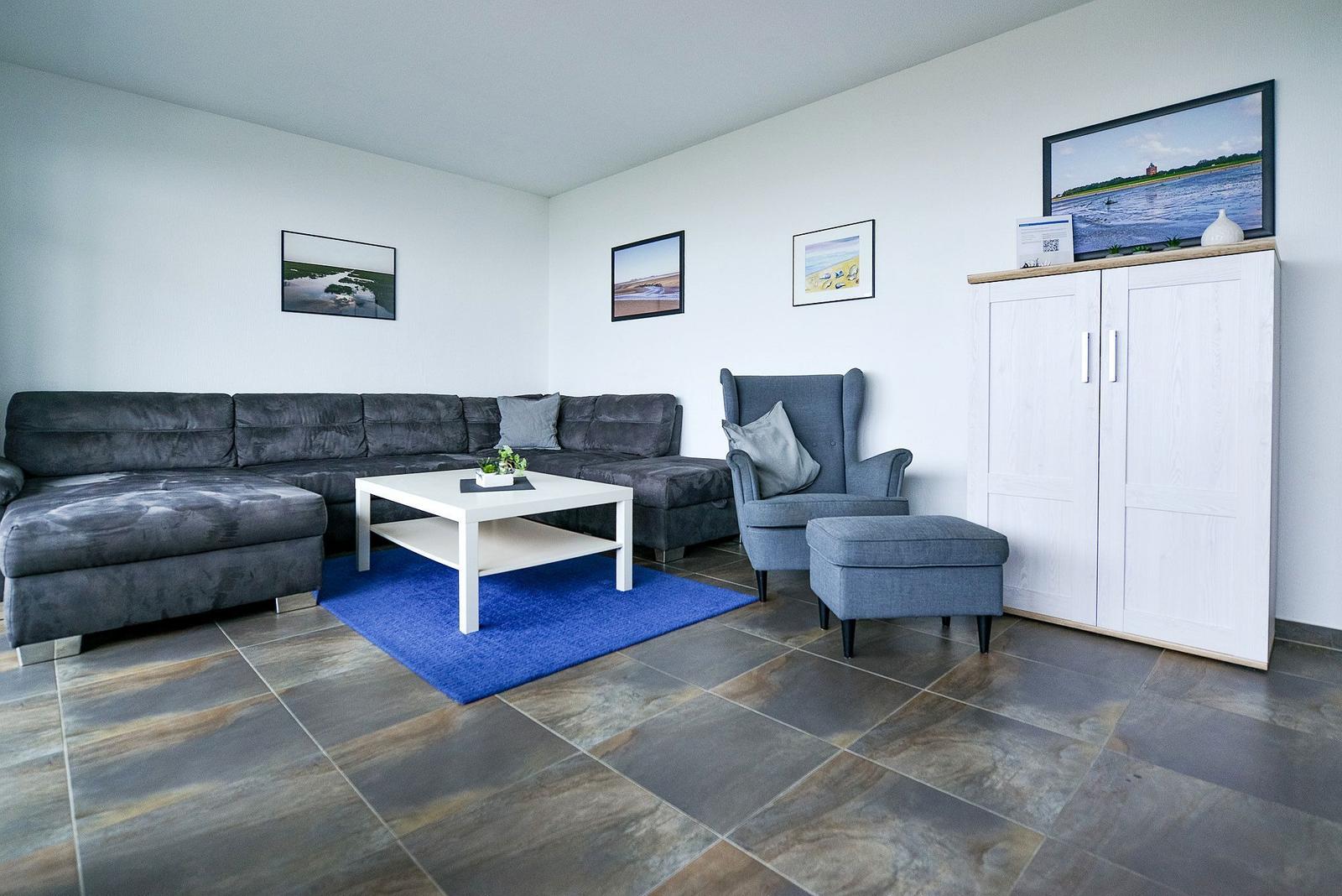 Wohnzimmer mit grauem Sofa, blauem Teppich und weißem Couchtisch.
