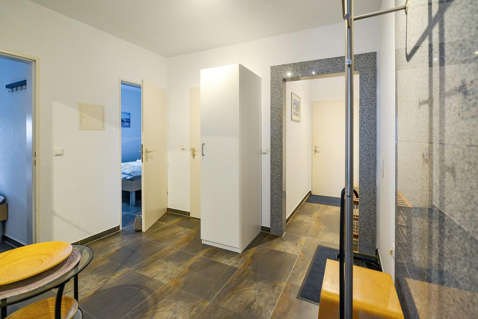 Flur mit Garderobe, Schlafzimmer und Dusche. Bodenfliesen und Holzmöbel.