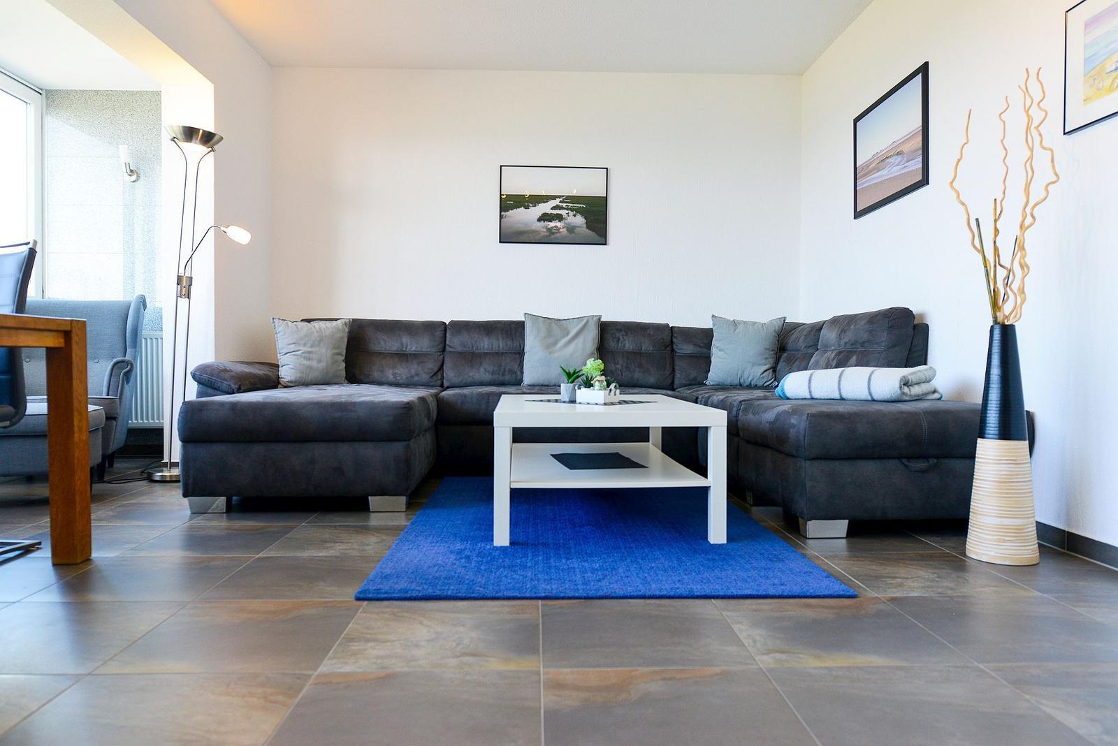 Wohnzimmer mit grauem Sofa, weißem Tisch und blauem Teppich.