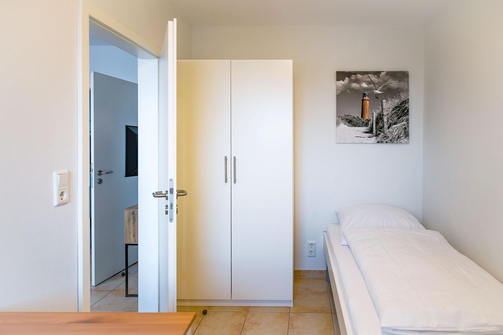 Schlafzimmer mit Einzelbett, Kleiderschrank und Wandbild. Tür führt in angrenzenden Raum.