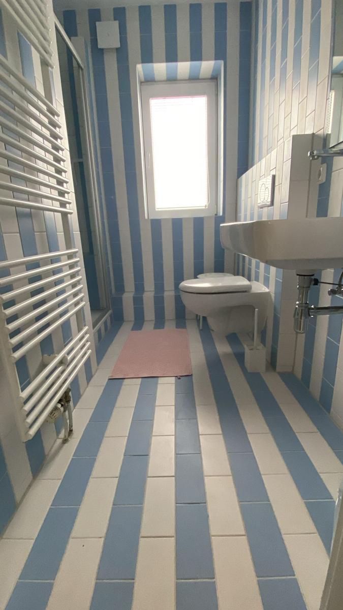 Badezimmer mit blau-weiß gestreiften Fliesen, Toilette, Waschbecken und Dusche.