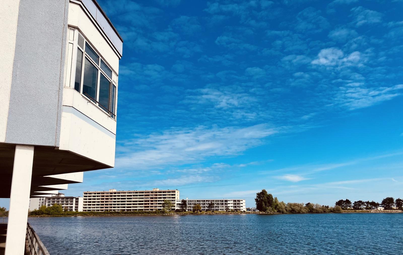 Wohnung mit Blick auf Wasser und gegenüberliegendes Gebäude unter blauem Himmel.