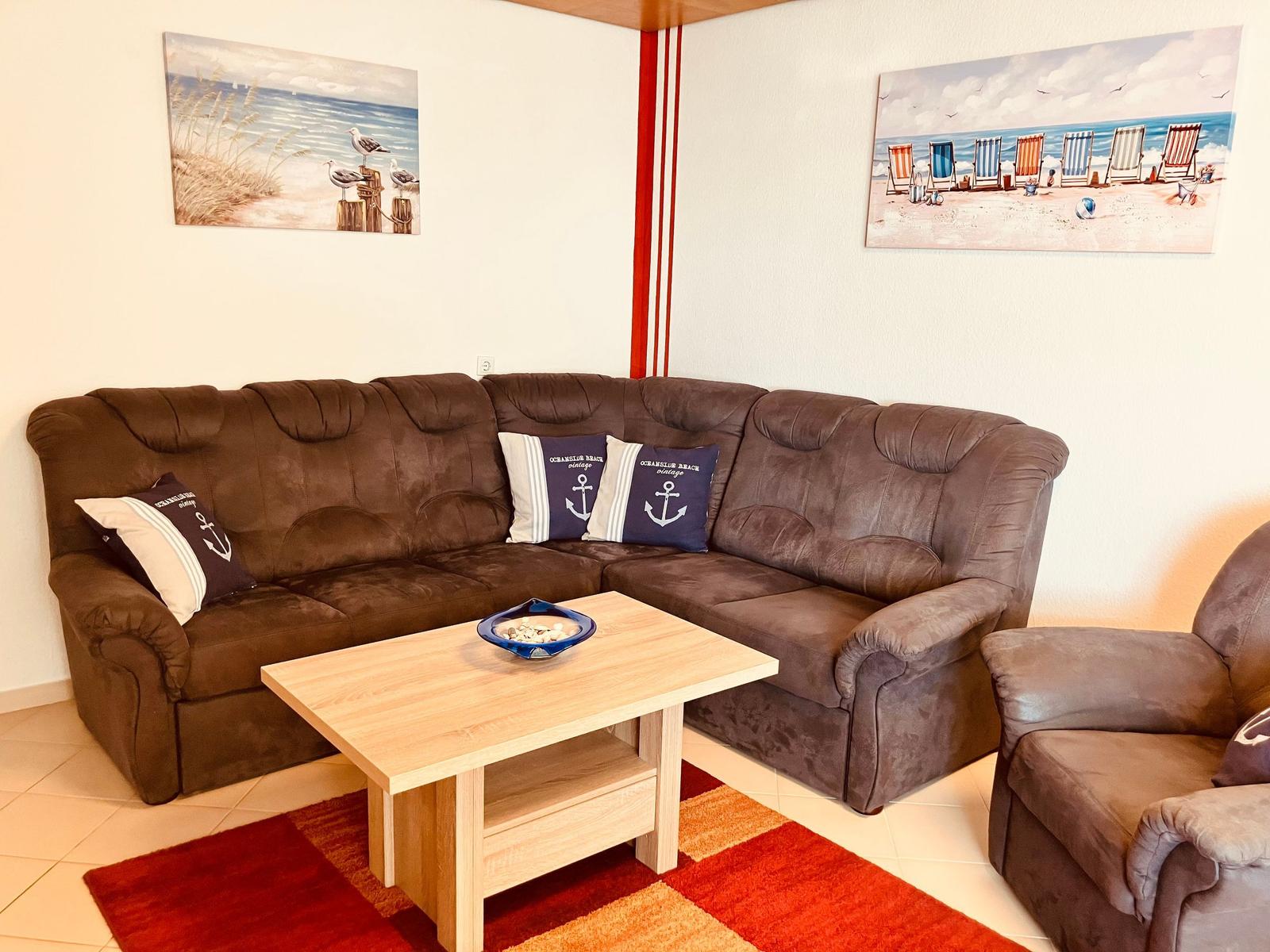 Ein Wohnzimmer mit braunem Sofa, Holztisch und Strandbildern an den Wänden.