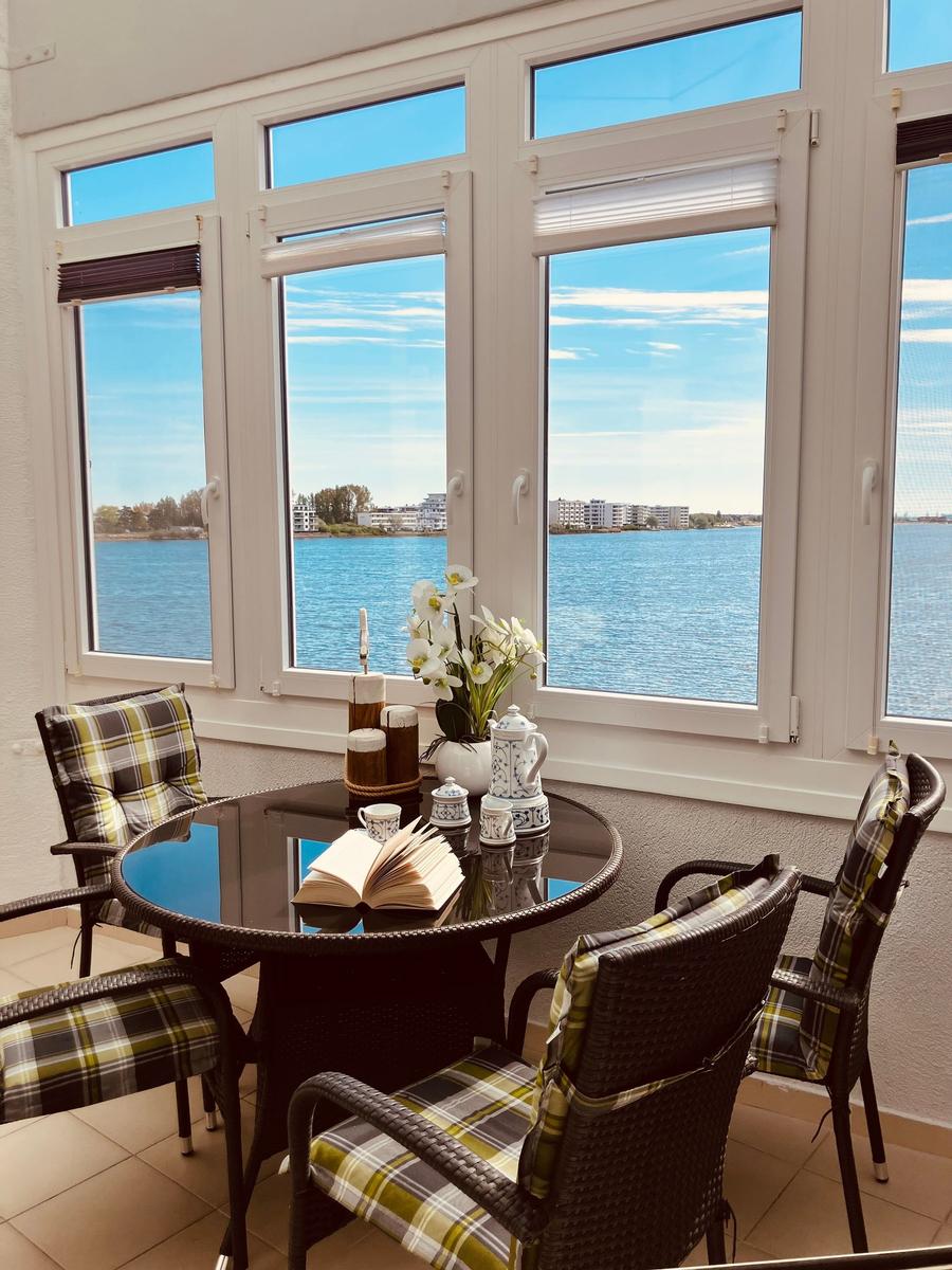 Rundtisch mit Stühlen und Blick auf Wasser. Blumen und Teekanne auf Tisch.