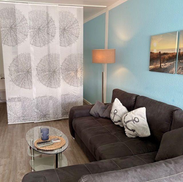 Ein Wohnzimmer mit braunem Sofa, Tisch und Vorhang mit Muster.