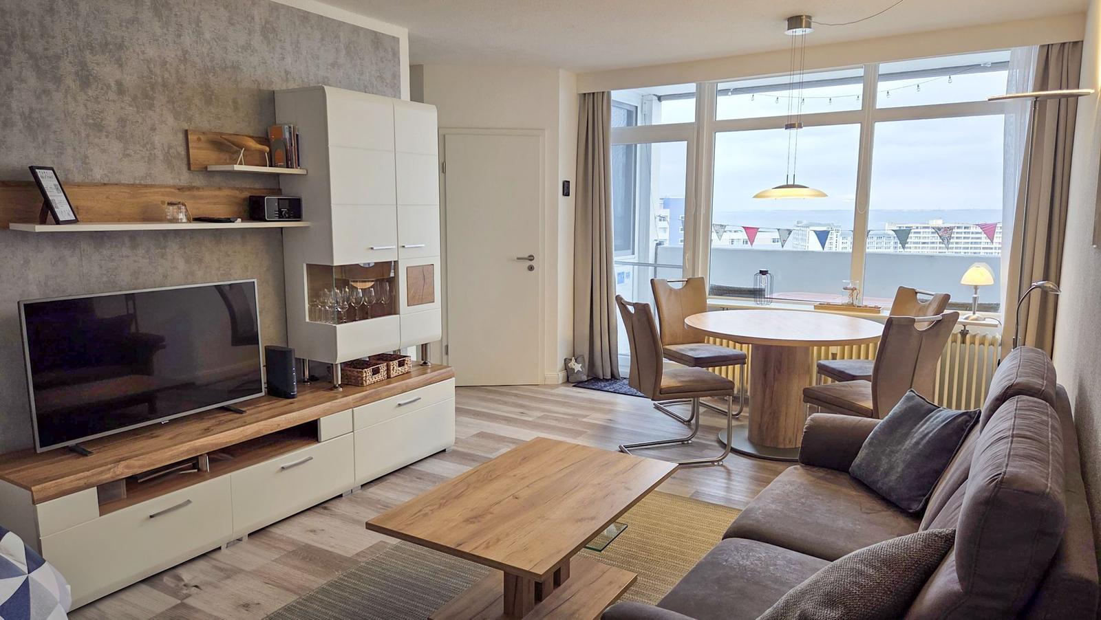 Living and dining area with sofa, table, and TV. Large windows with water view.