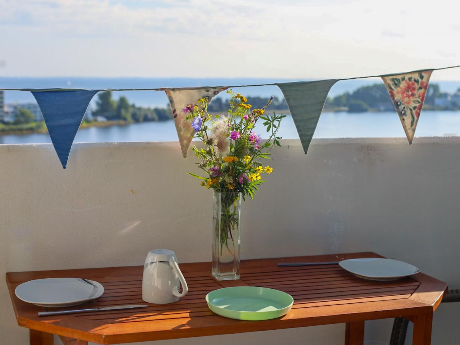 Table with plates, kettle, and flowers on balcony with sea view and bunting.