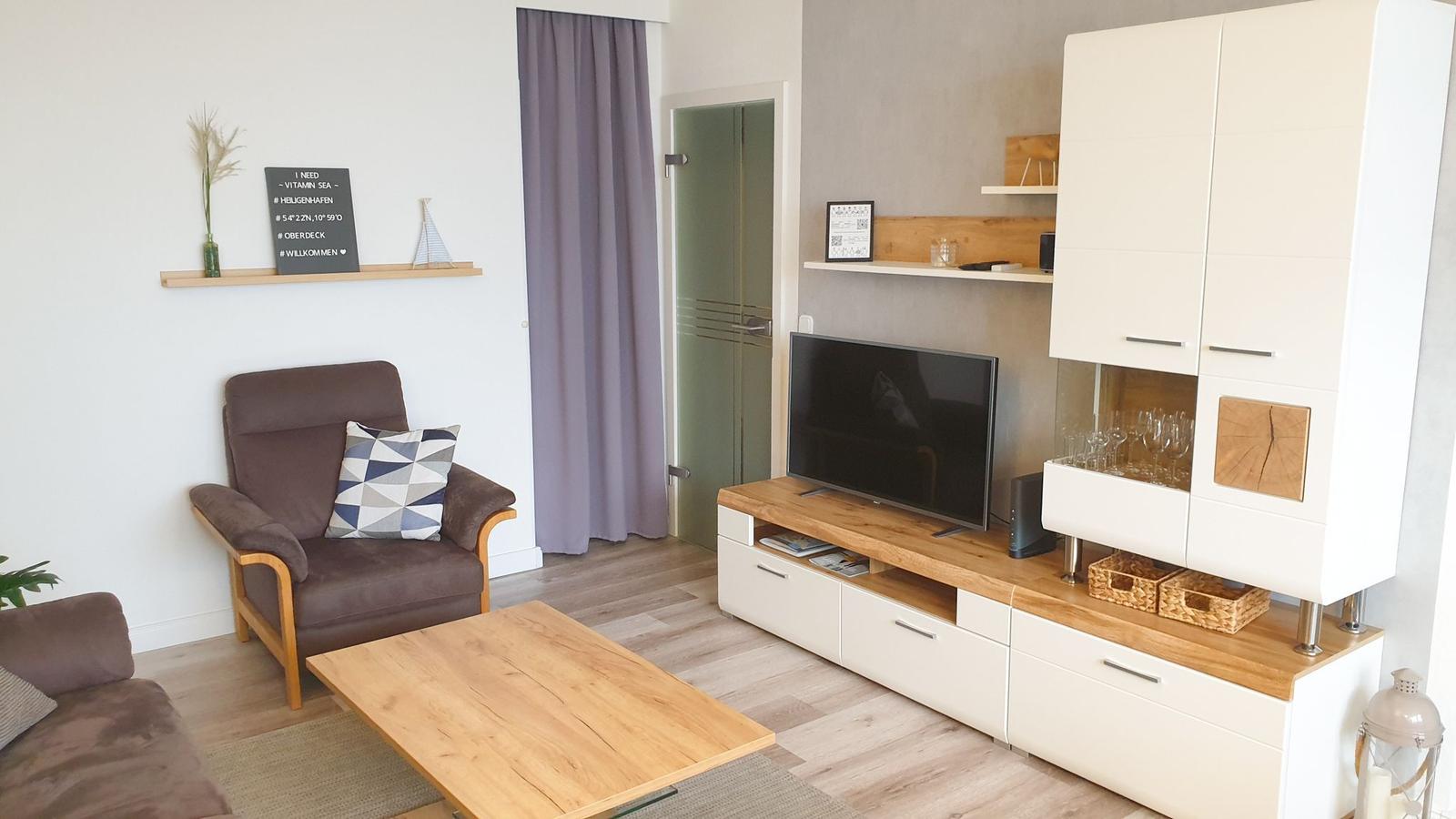 Living room with sofa, armchair, coffee table, and TV. Wooden floor and white cabinets.