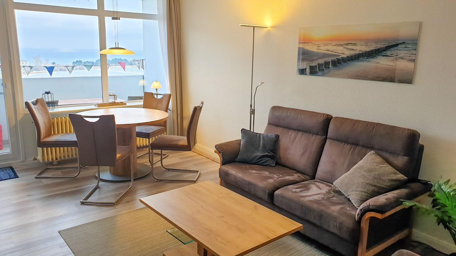 Living and dining area with sofa, table, and seating. View of water and sky.