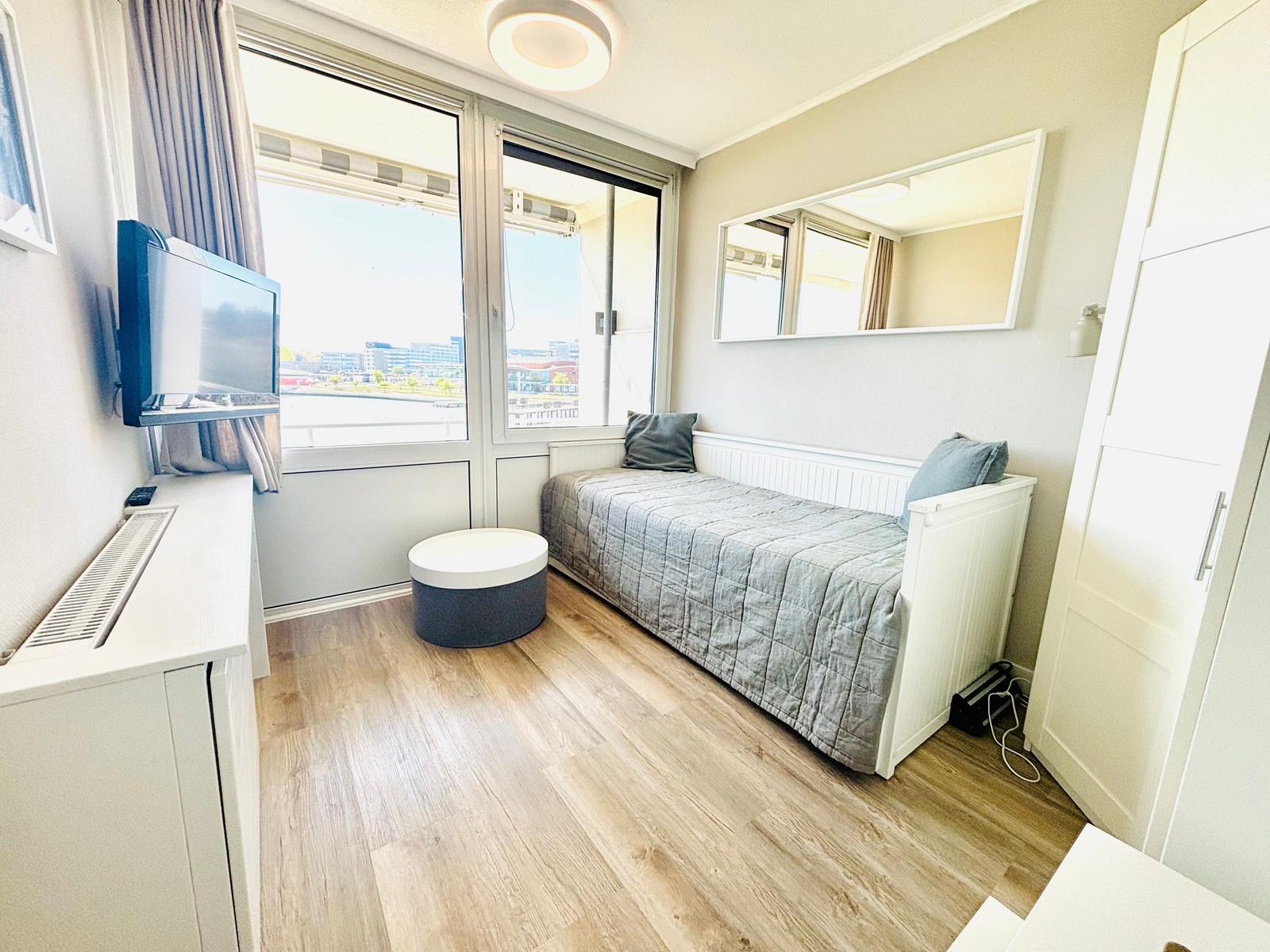 Zimmer mit Bett, TV und großem Fenster mit Blick auf die Stadt.