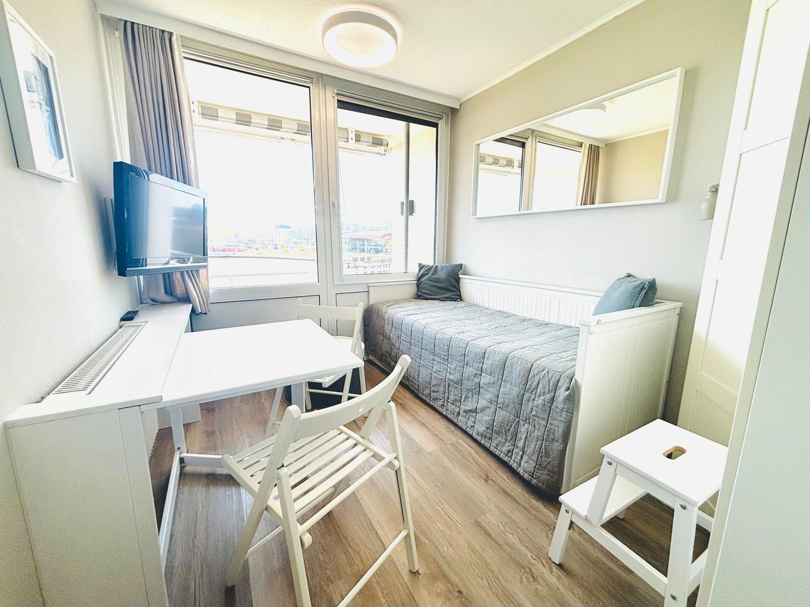 Zimmer mit Bett, Tisch, Stühlen und Fernseher. Fenster mit Blick auf Außenbereich.