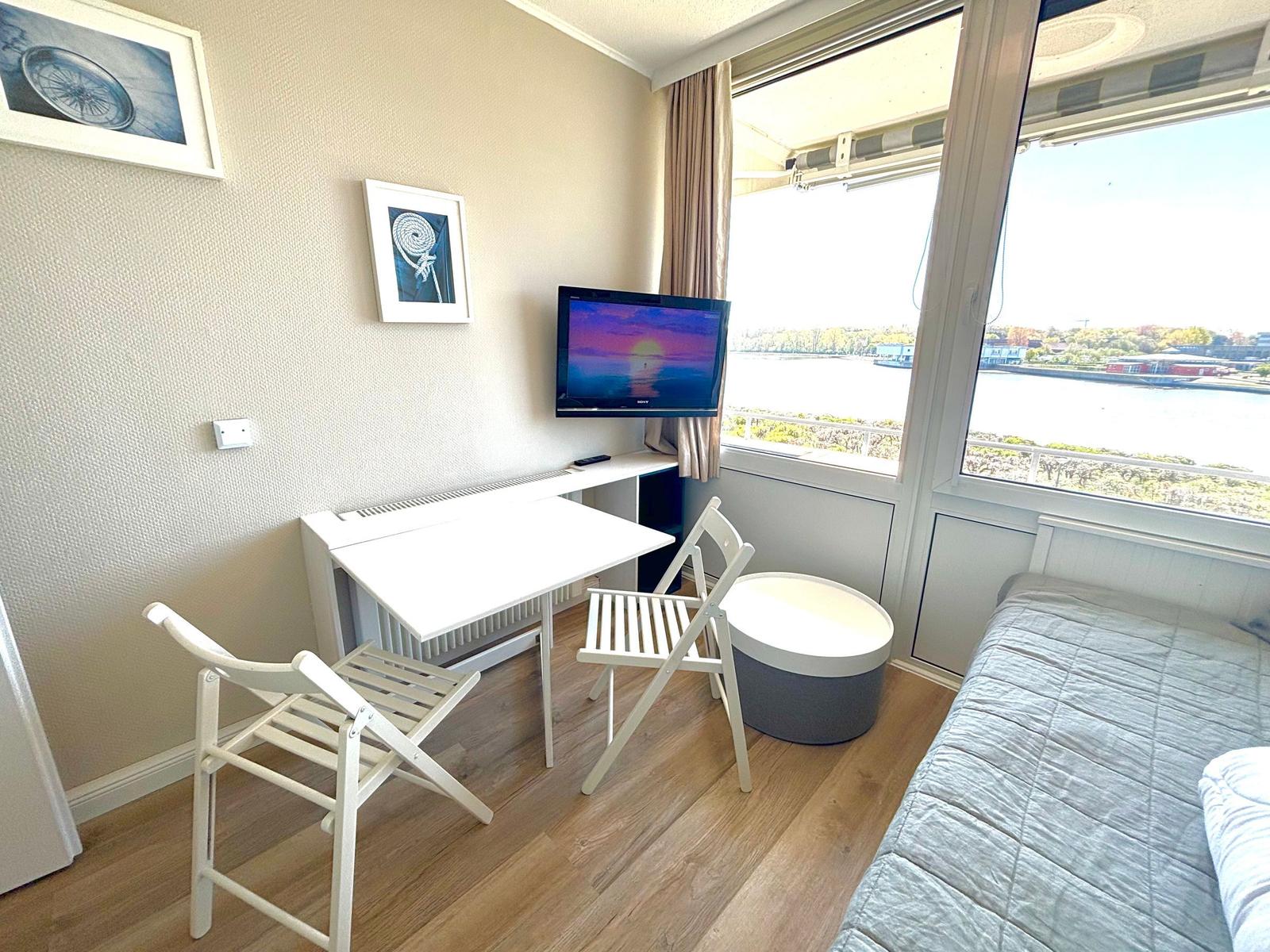 Zimmer mit Bett, Schreibtisch, TV und Fensterblick auf Wasser.