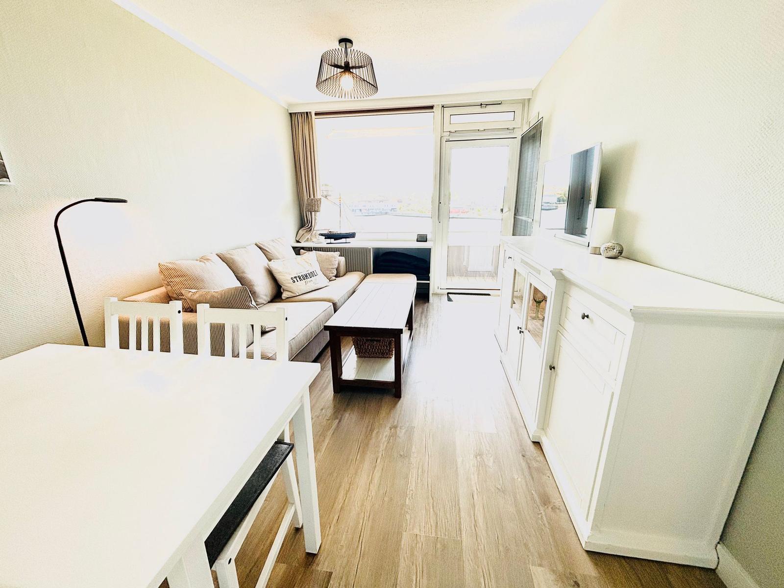 Wohnzimmer mit Sofa, Esstisch und TV-Schrank. Holzboden und Fenster zur Aussicht.