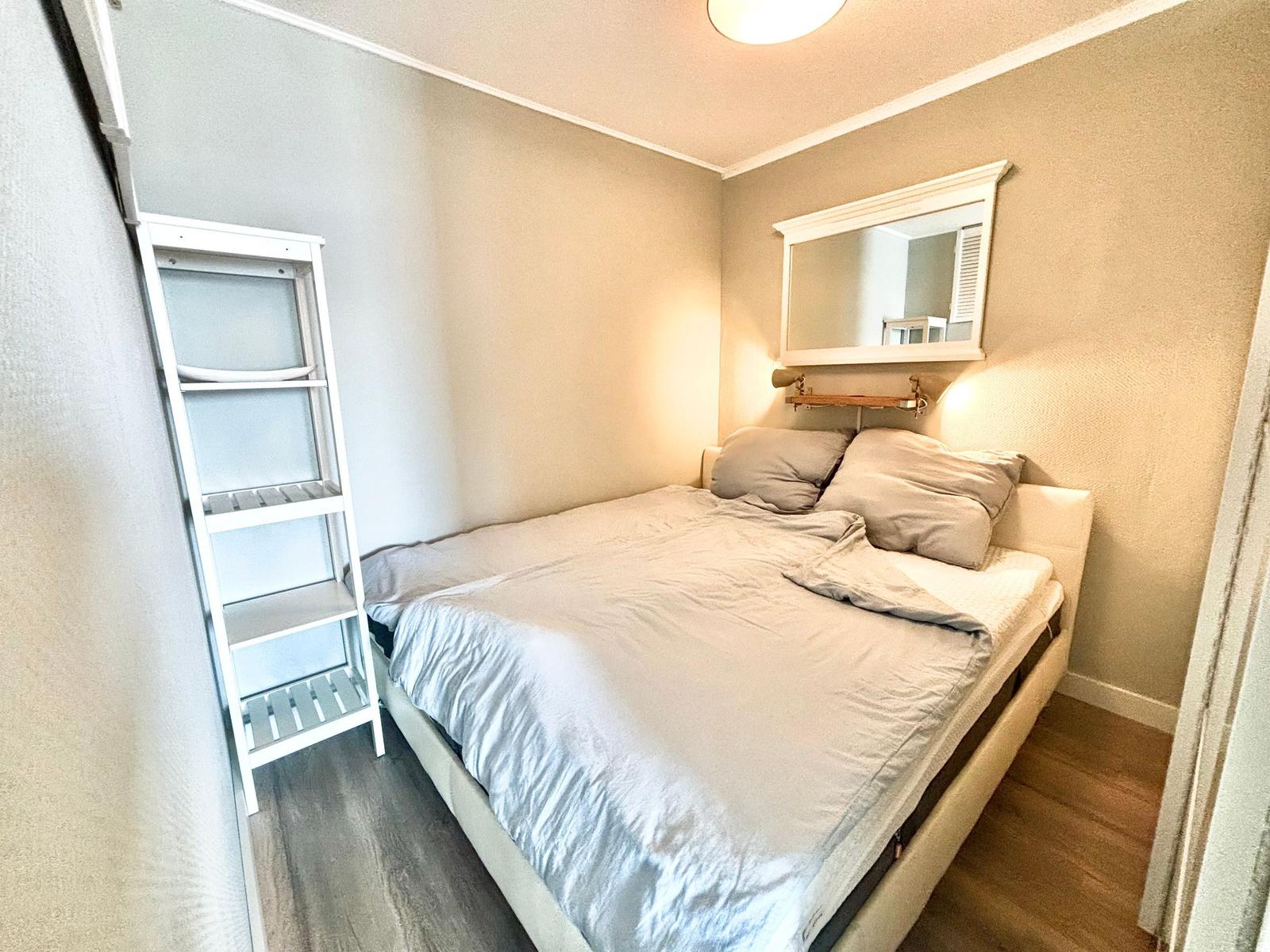 Schlafzimmer mit Bett, Spiegel und weißem Regal.