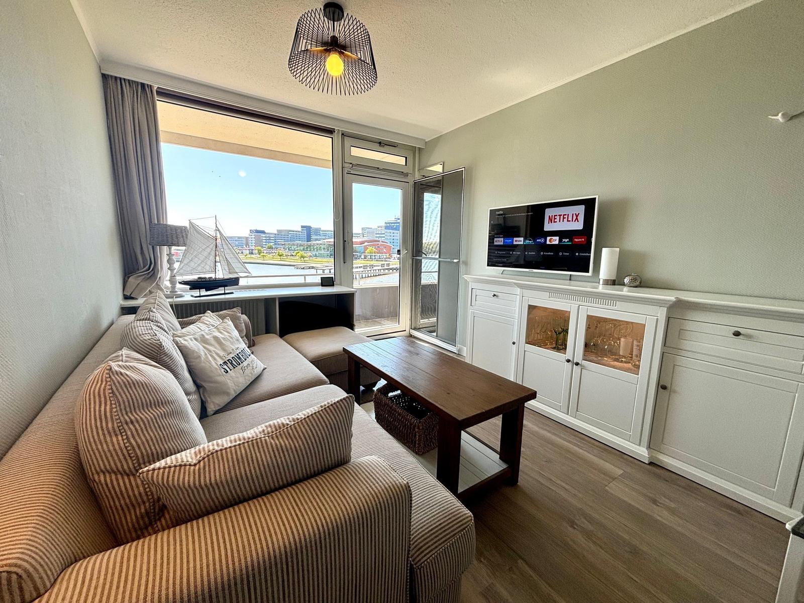 Wohnzimmer mit Sofa, Fernseher und Blick auf Wasser.