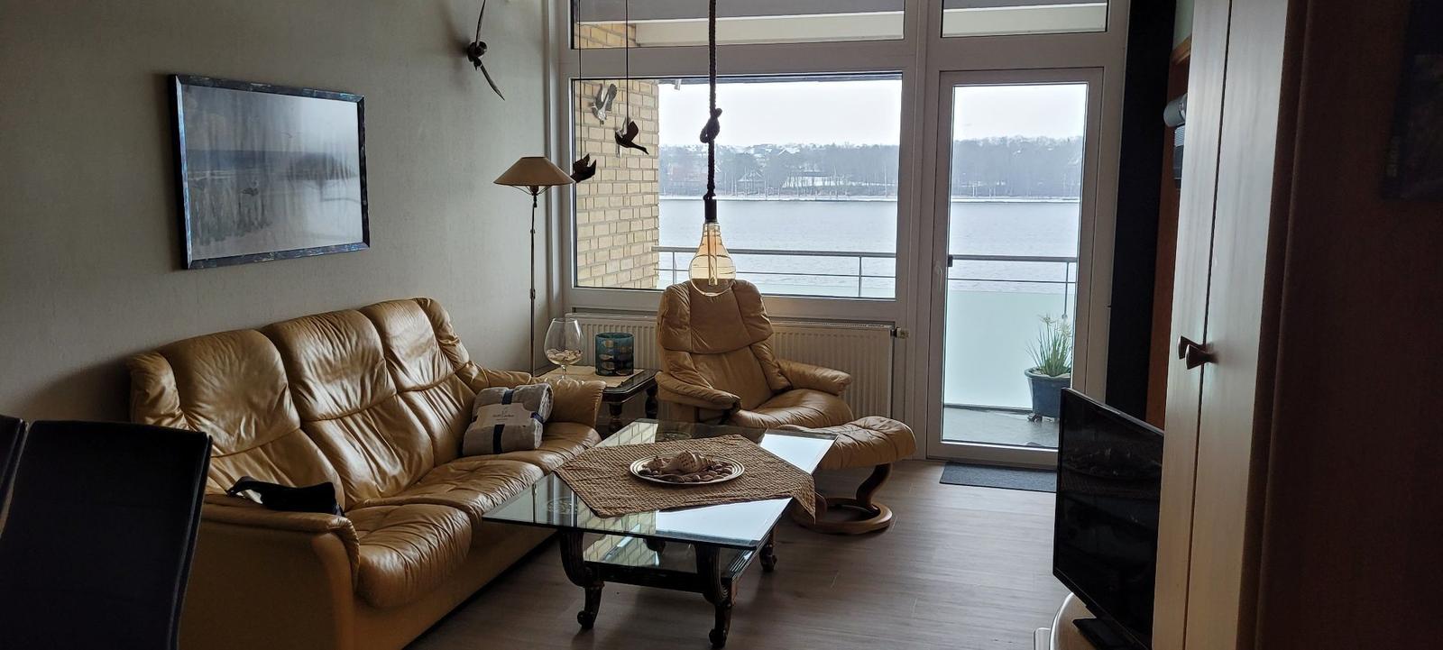 Wohnzimmer mit Ledersofa, Sessel und Blick auf Wasser