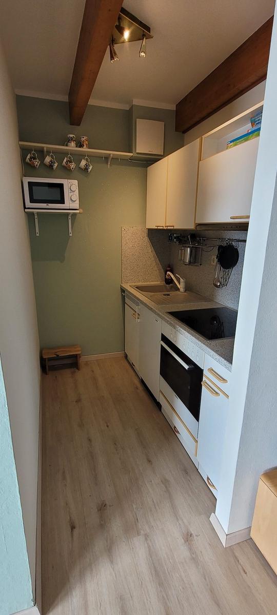 Küche mit weißen Schränken, Herd, Spüle und Mikrowelle an der Wand.
