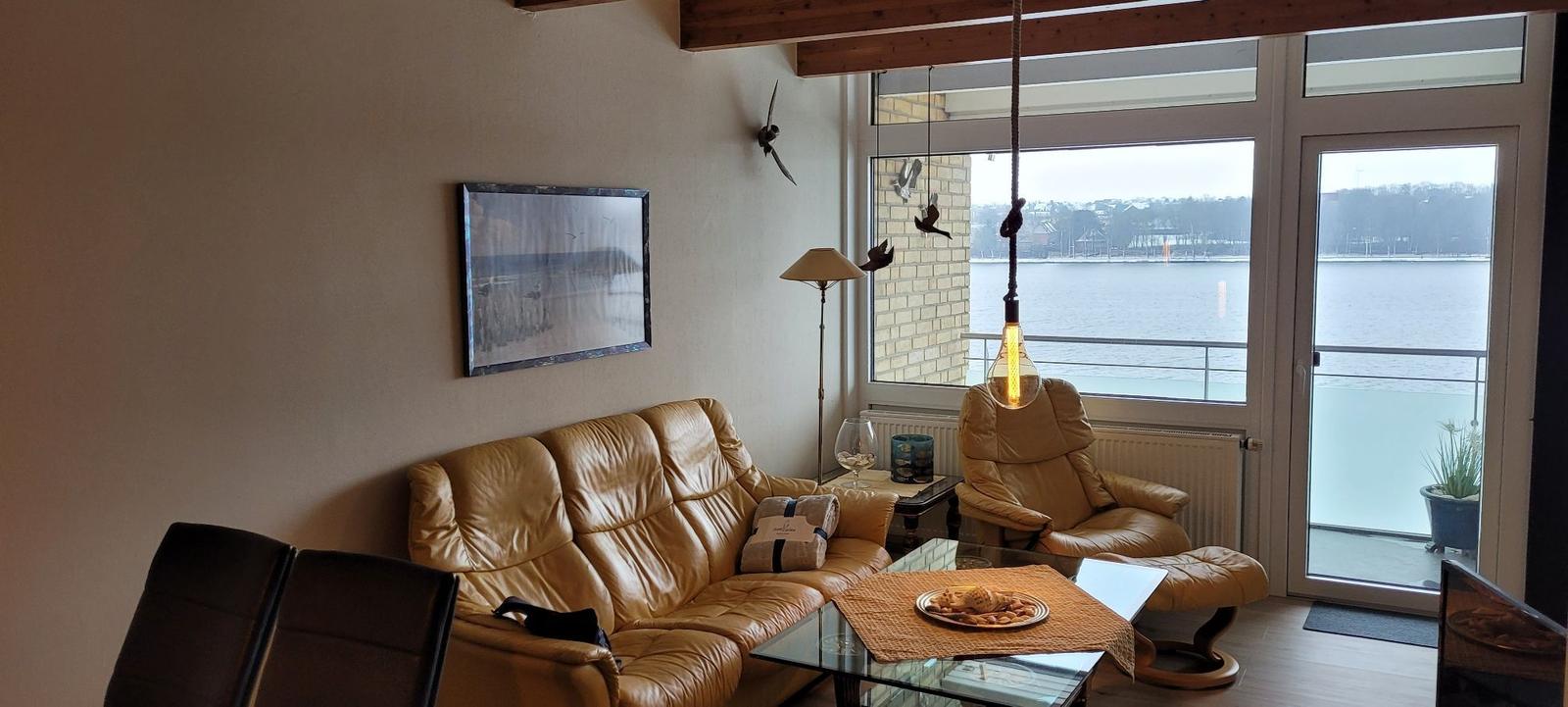Wohnzimmer mit Ledersofa, Sessel und Blick auf Wasser