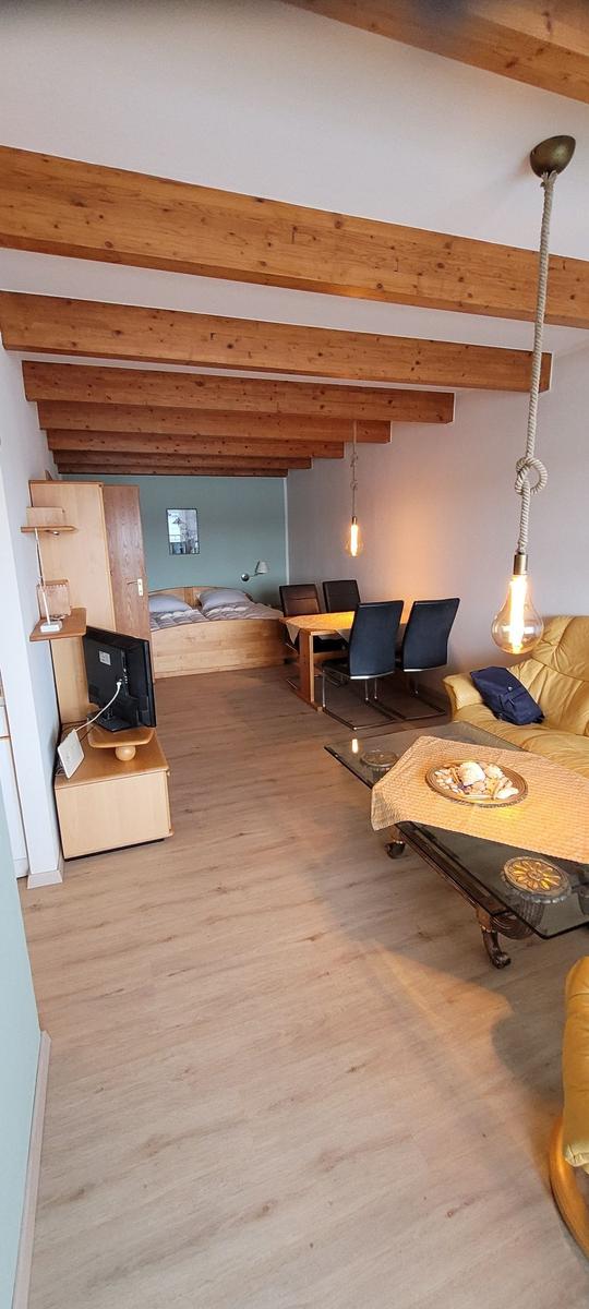 Wohnung mit Essbereich, Sofa und Bett. Holzbalken an der Decke.