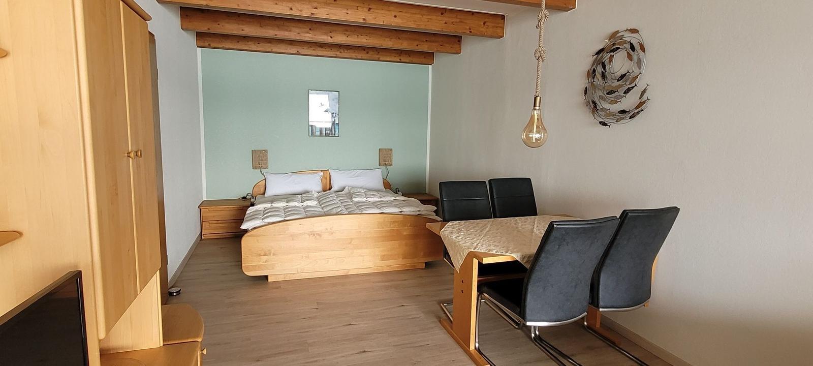 Schlafzimmer mit Bett, Tisch und Stühlen. Holzdecken und Wandgestaltung.