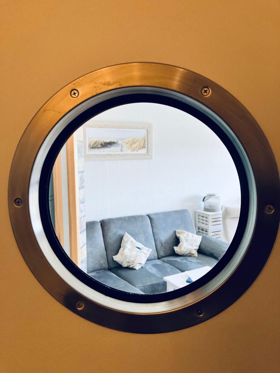 Durch ein runden Fenster ist ein Wohnbereich mit Sofa und Wandbild sichtbar.