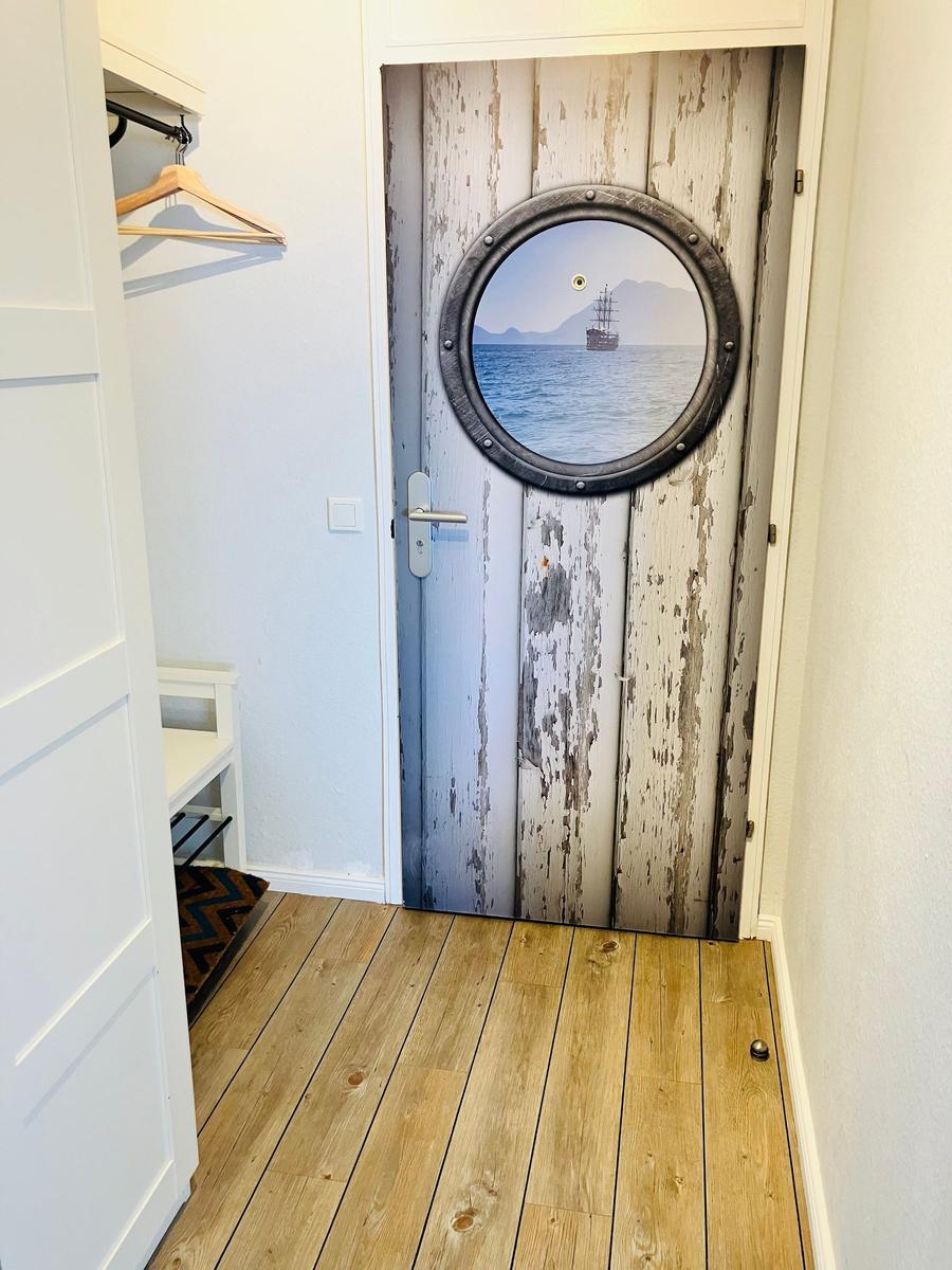 Tür mit Rundfenster zeigt Schiff auf Meer. Holzfußboden und Kleiderschrank sichtbar.