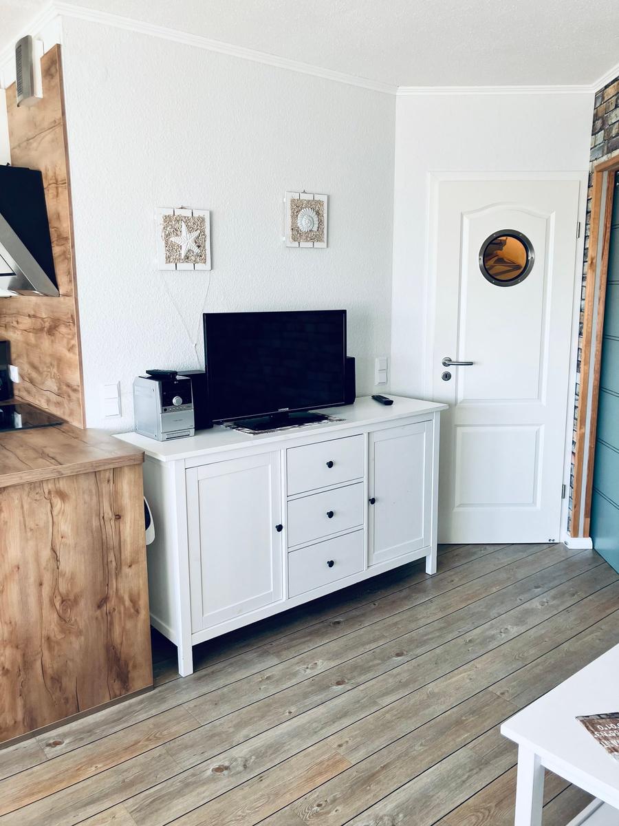 Wohnbereich mit TV-Schrank, Holzboden und Küchenzeile.