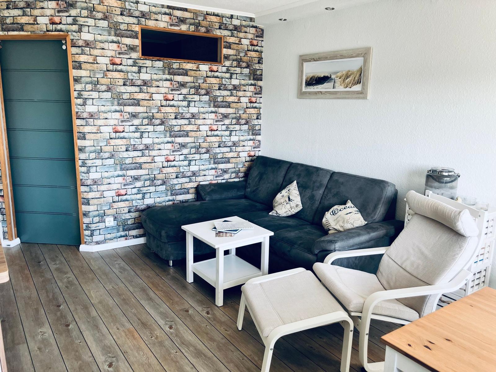 Wohnzimmer mit Sofa, Sessel und Holzboden. Wand mit Steinoptik und Fernseher.