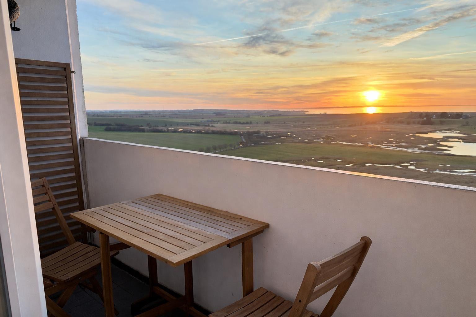 Terrasse mit Tisch und Stühlen. Blick auf Felder und Sonnenuntergang.