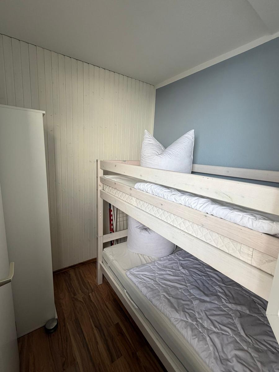 Zimmer mit Doppelstockbett, Holzboden und weißer Schrankwand.