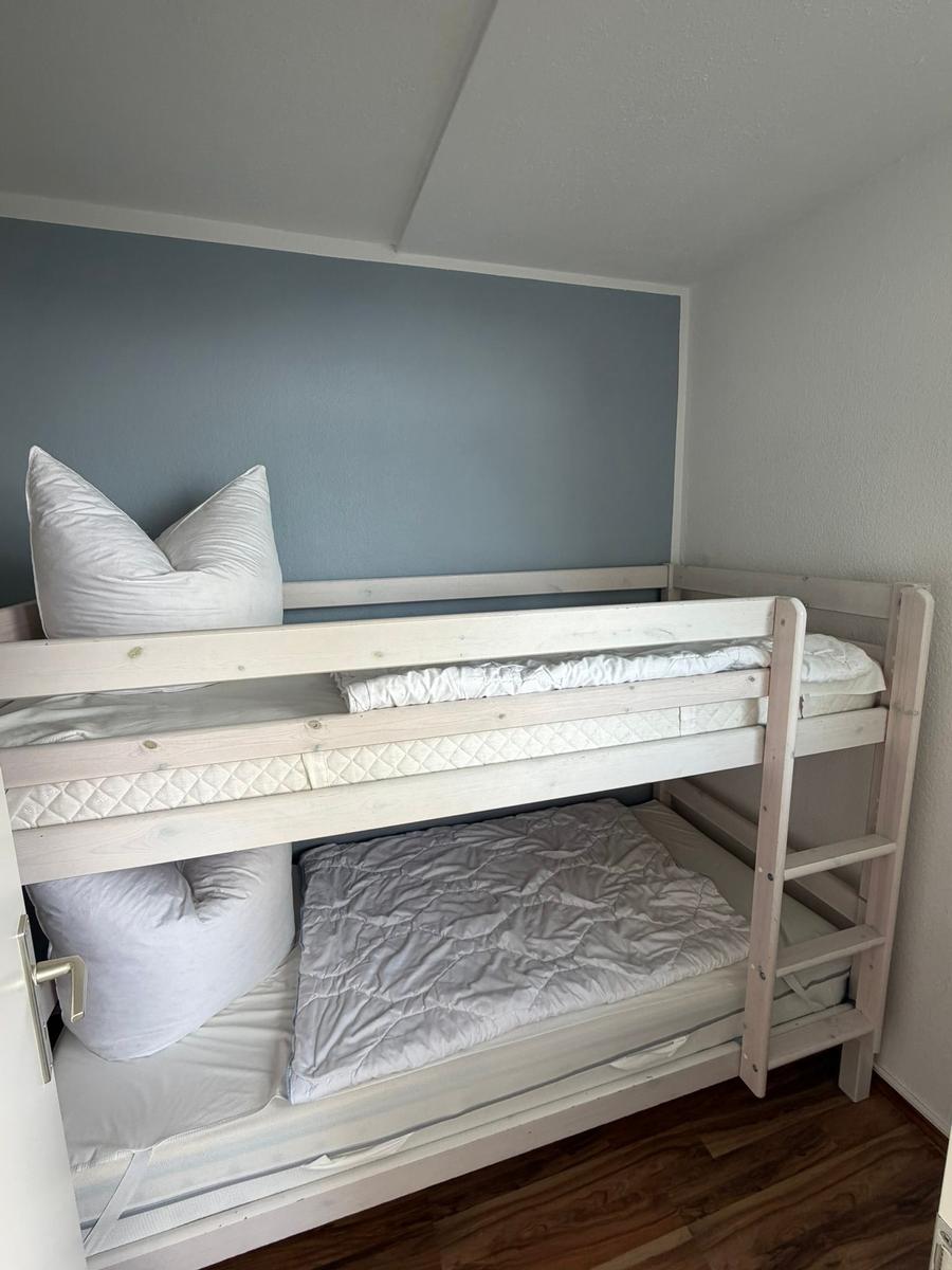 Doppelstockbett mit Matratzen und Kissen in einem Raum mit Holzboden und blauer Wand.
