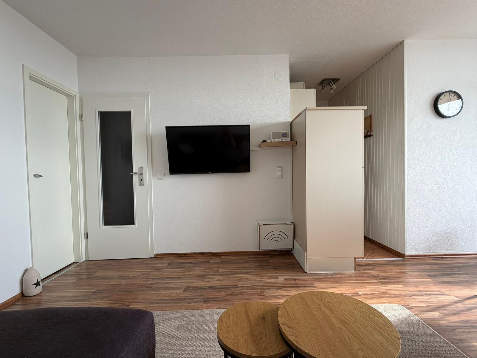 Wohnzimmer mit TV, Holzboden und zwei runden Tischen.
