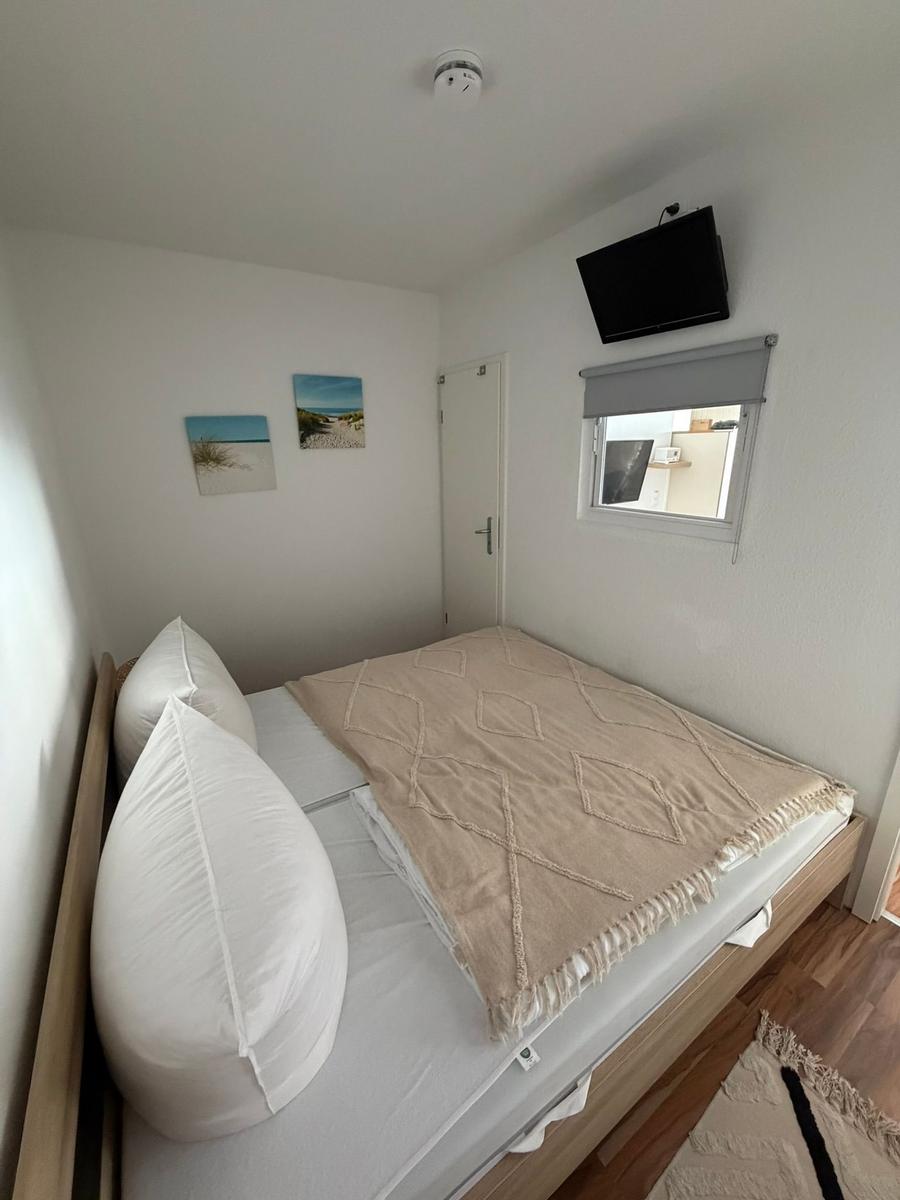 Schlafzimmer mit Bett, Wandbildern, TV und Fenster.