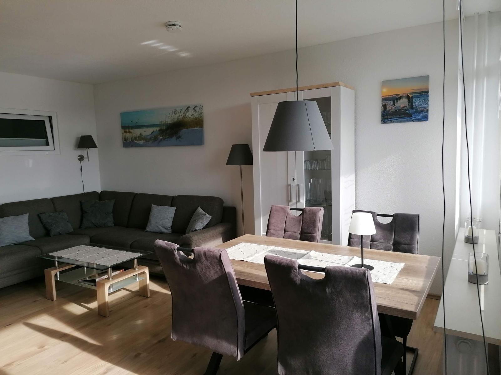 Living and dining area with sofa, table, and chairs. Wall art and lighting visible.
