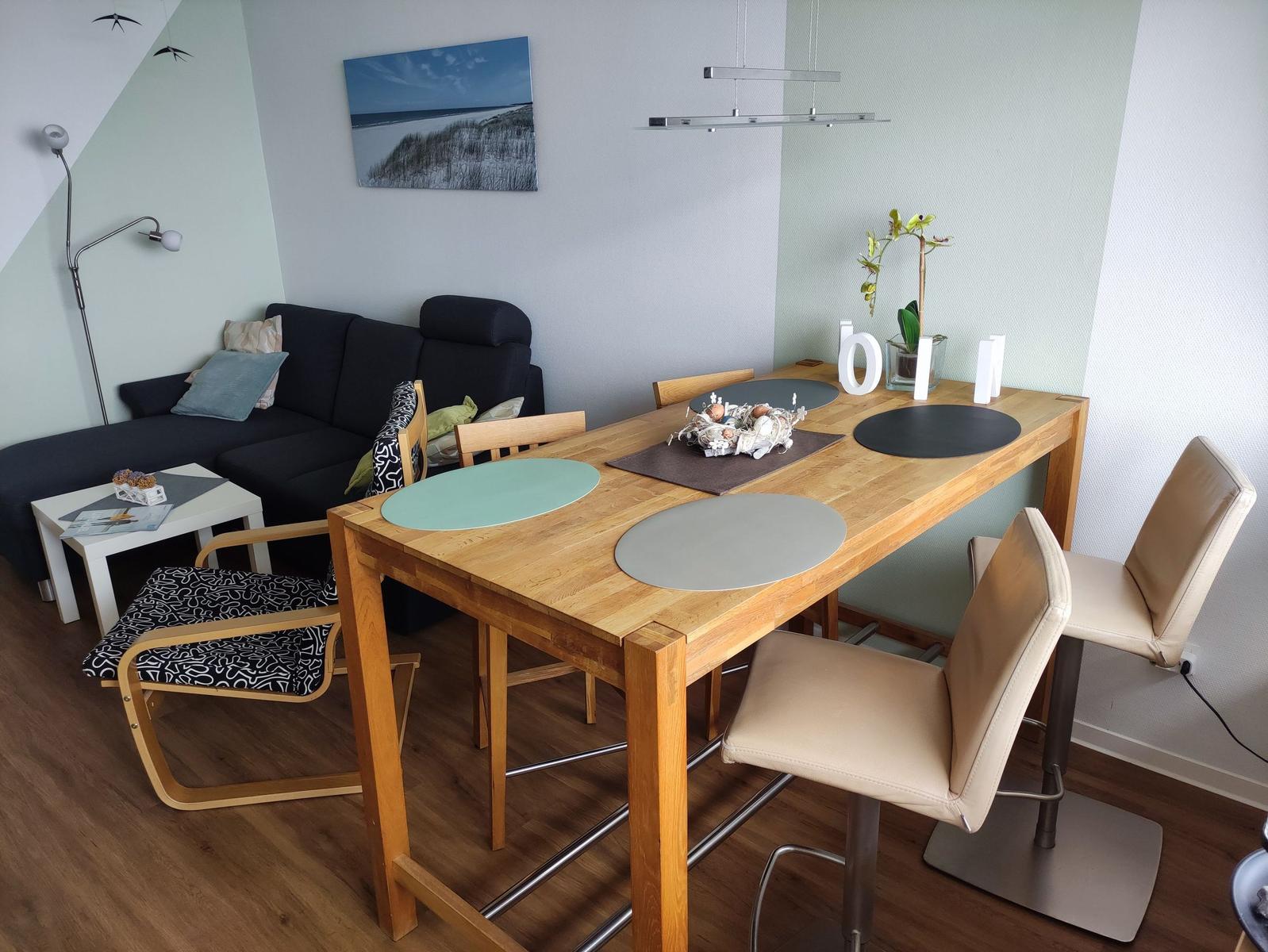 Essbereich mit Holztisch und Stühlen, Sofa und Wandbild im Hintergrund.