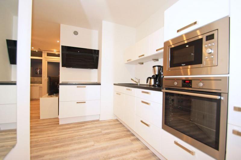 Kitchen with white cabinets, stainless steel oven and microwave. Wooden floor, view into living area.