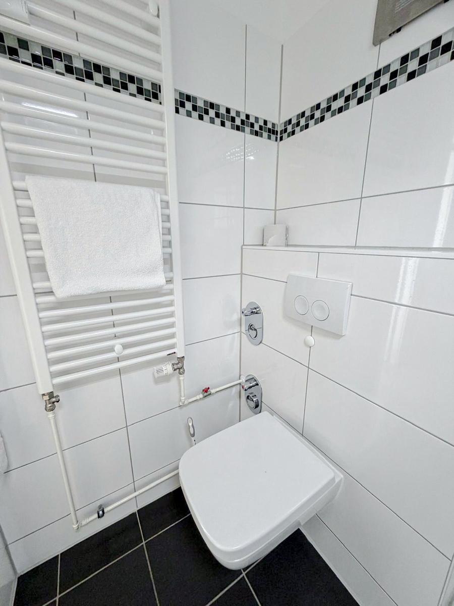 Bad mit Toilette, Heizkörper und Mosaikfliesen an der Wand.