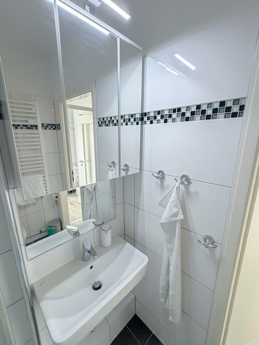 Badezimmer mit Waschbecken, Spiegel und Handtuchhalter an der Wand.