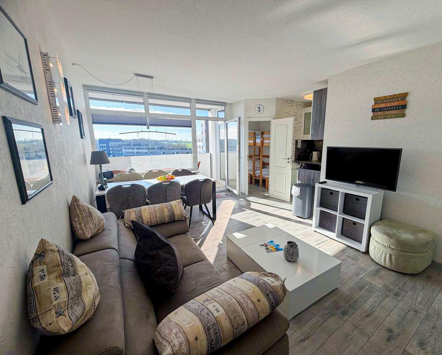 Wohnzimmer mit Sofa, Couchtisch und TV. Durchgang zur Küche und Schlafzimmer.