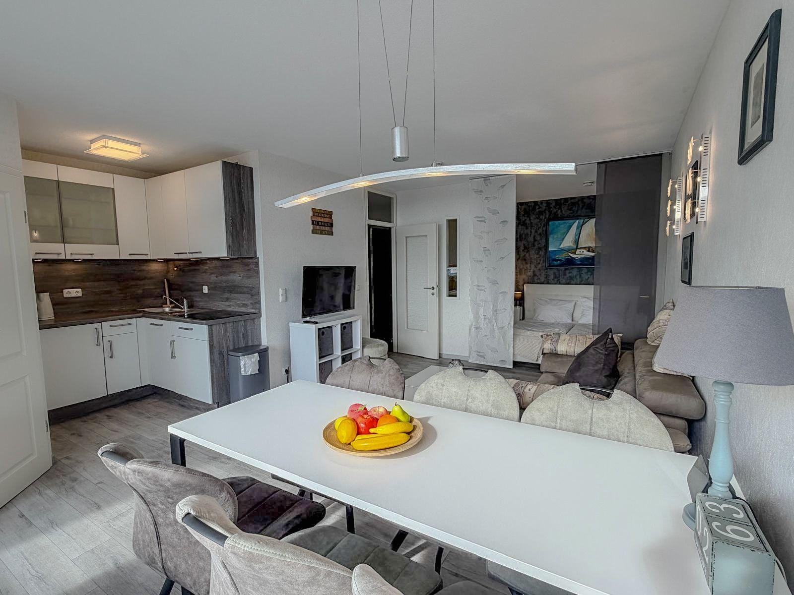 Wohnung mit Küche, Essbereich und Schlafzimmer im Hintergrund.