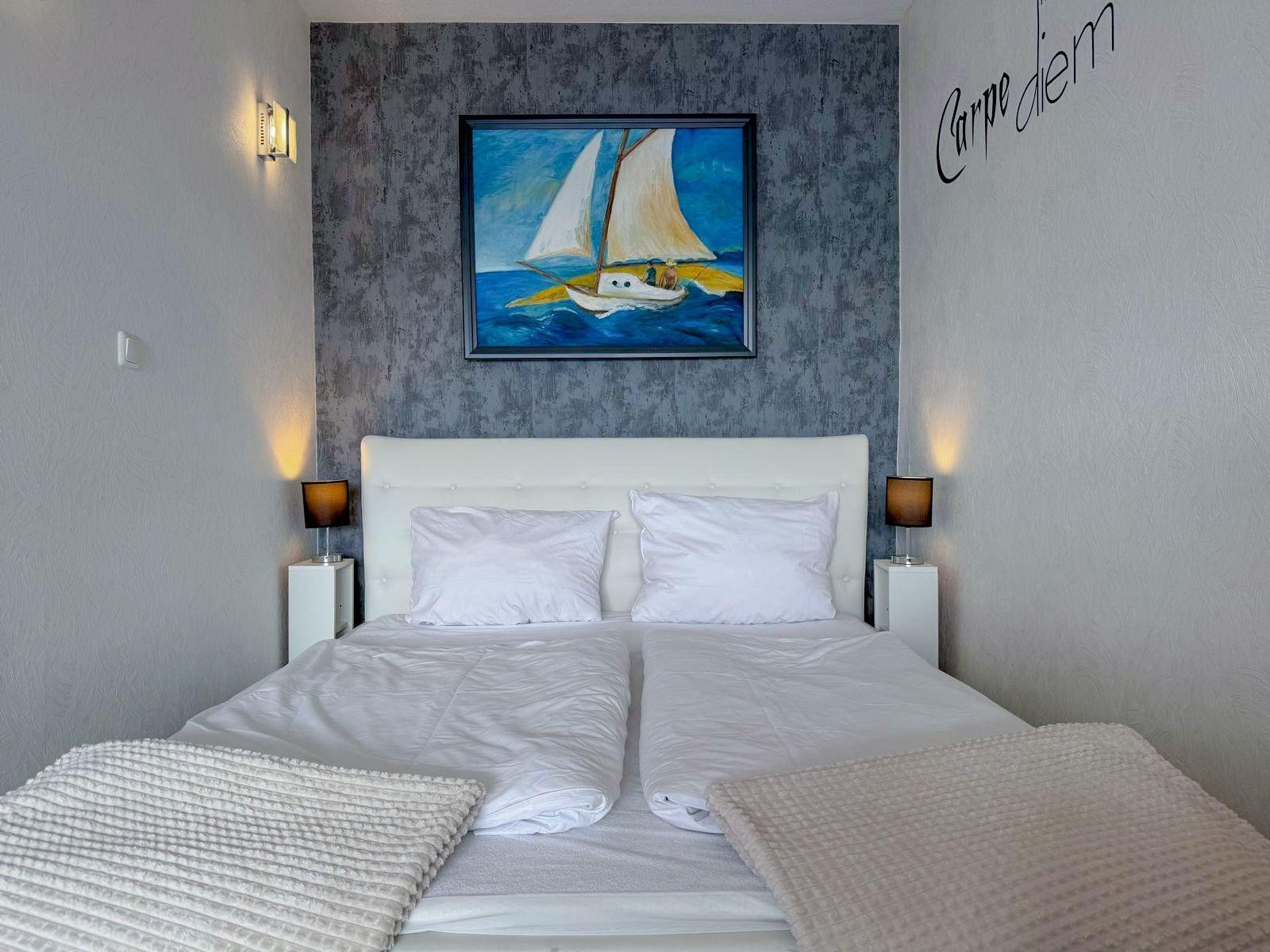Schlafzimmer mit weißem Bett, Wandbild mit Segelyacht und Wanddekoration.