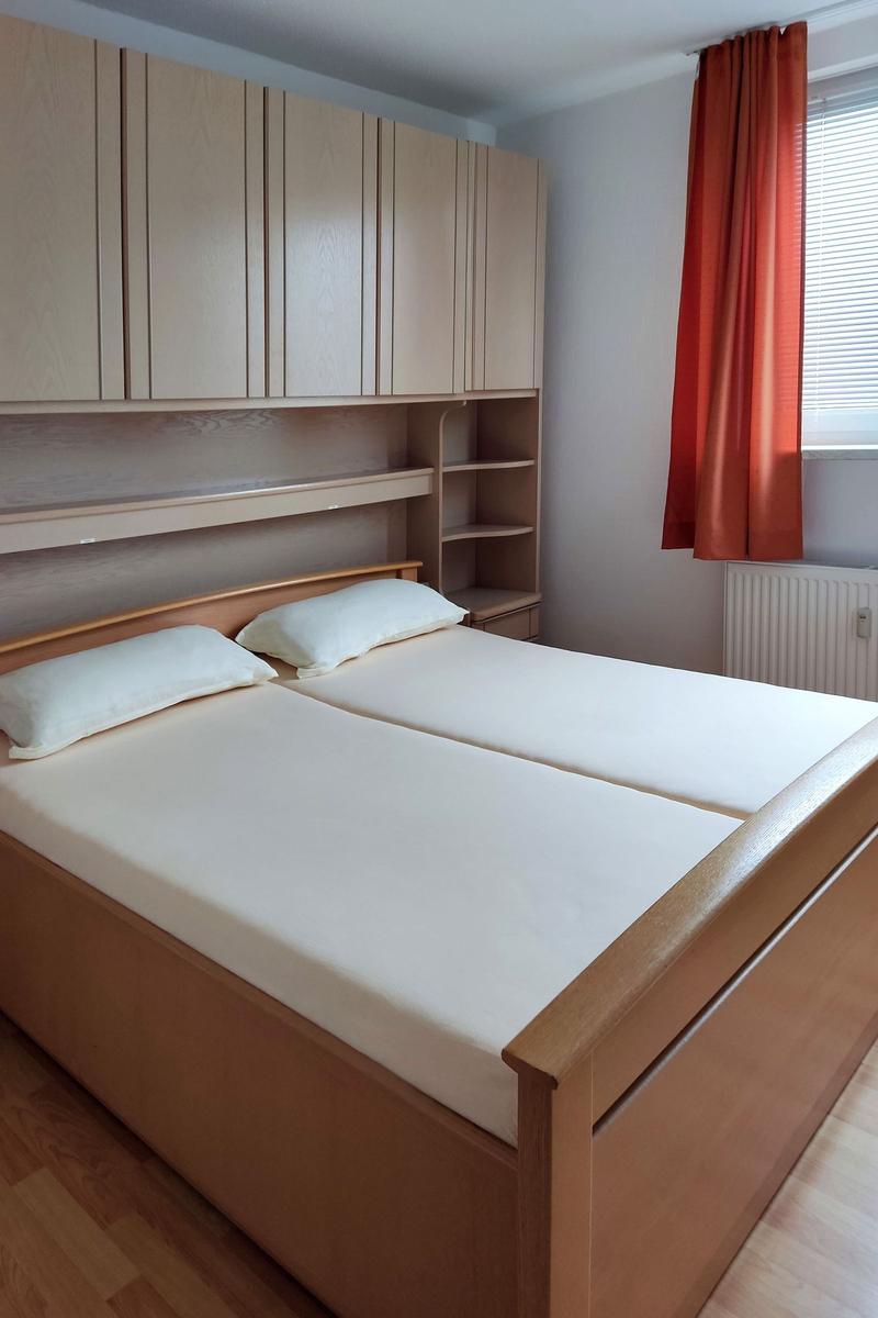 Bedroom with double bed, wooden furniture, and window with orange curtains.