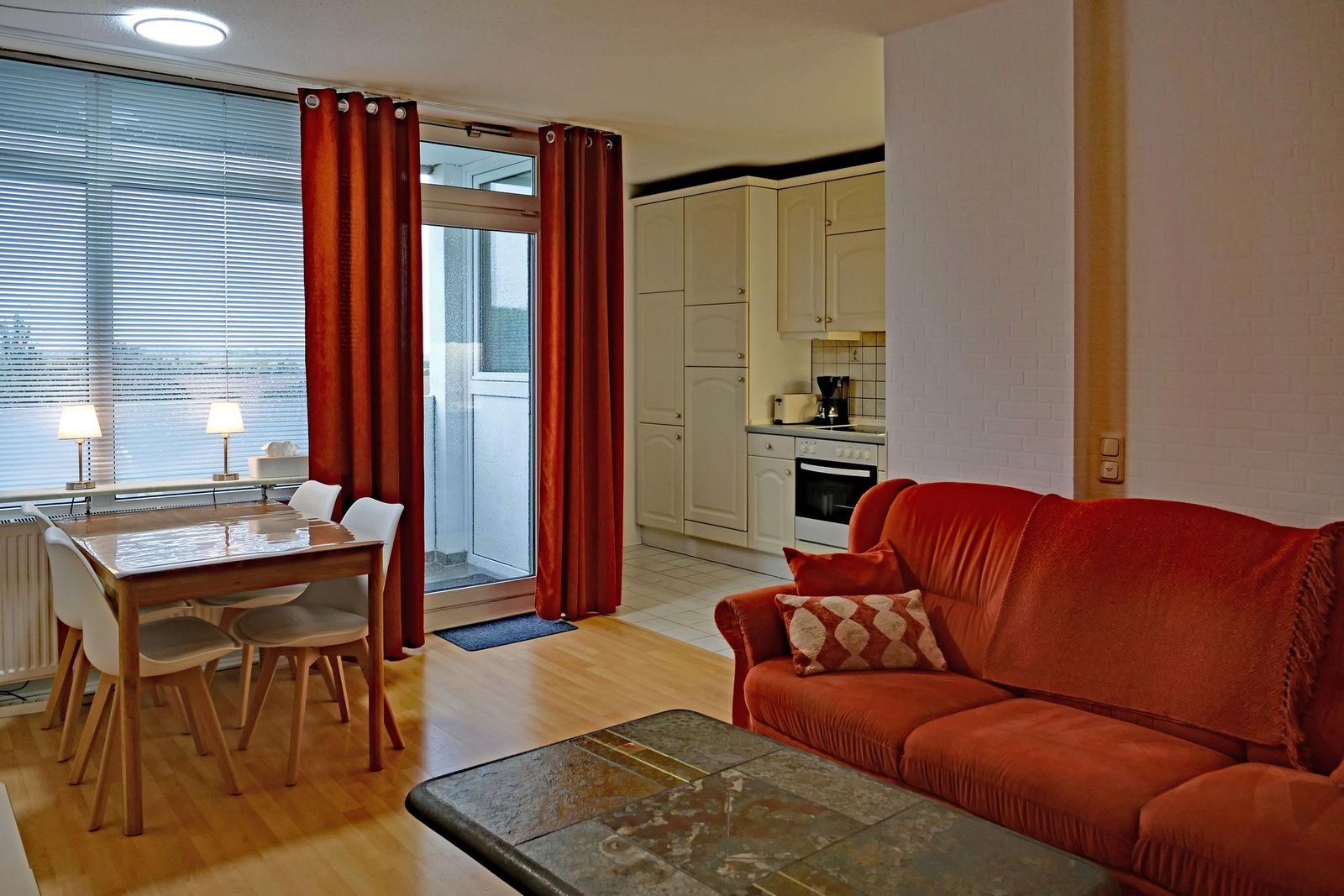Living area with red sofa, dining table, and kitchenette.
