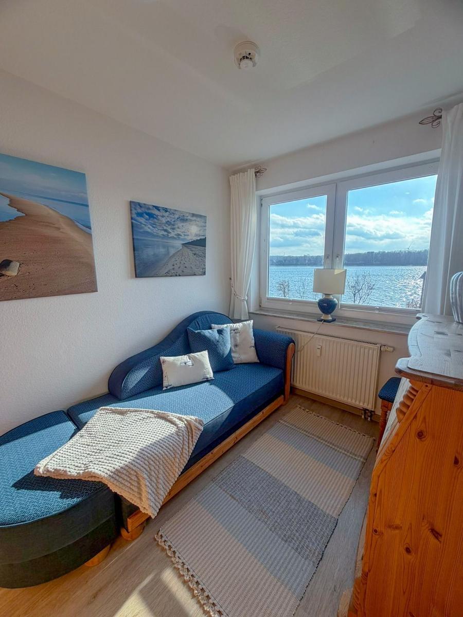 A room with a sofa, water view from the window, and wall pictures.