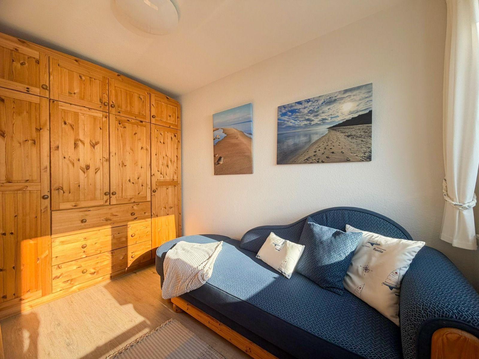 Bedroom with wooden wardrobe and sofa with cushions and blanket.