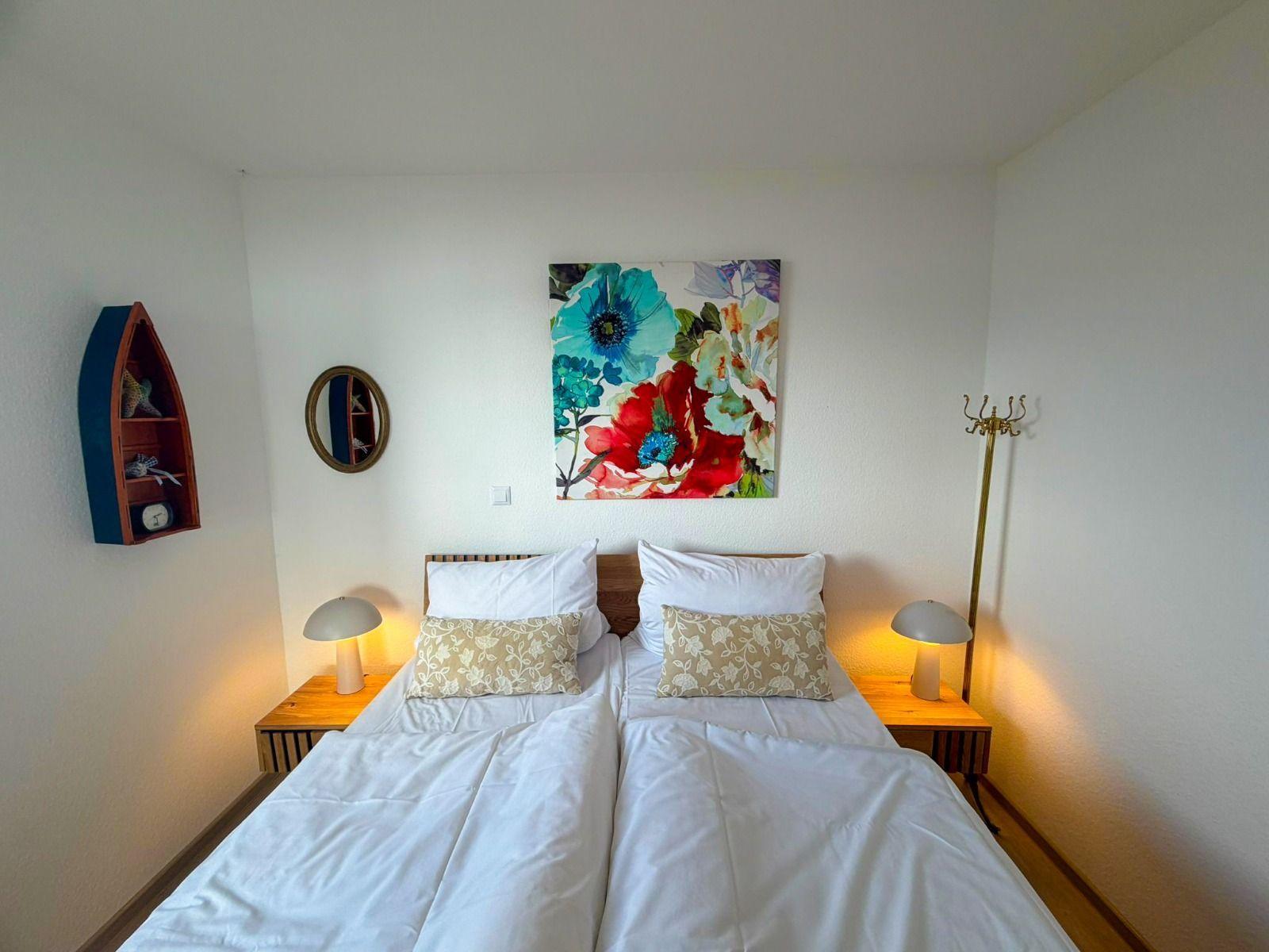 Room with double bed, nightstands, wall art, and decorative items.
