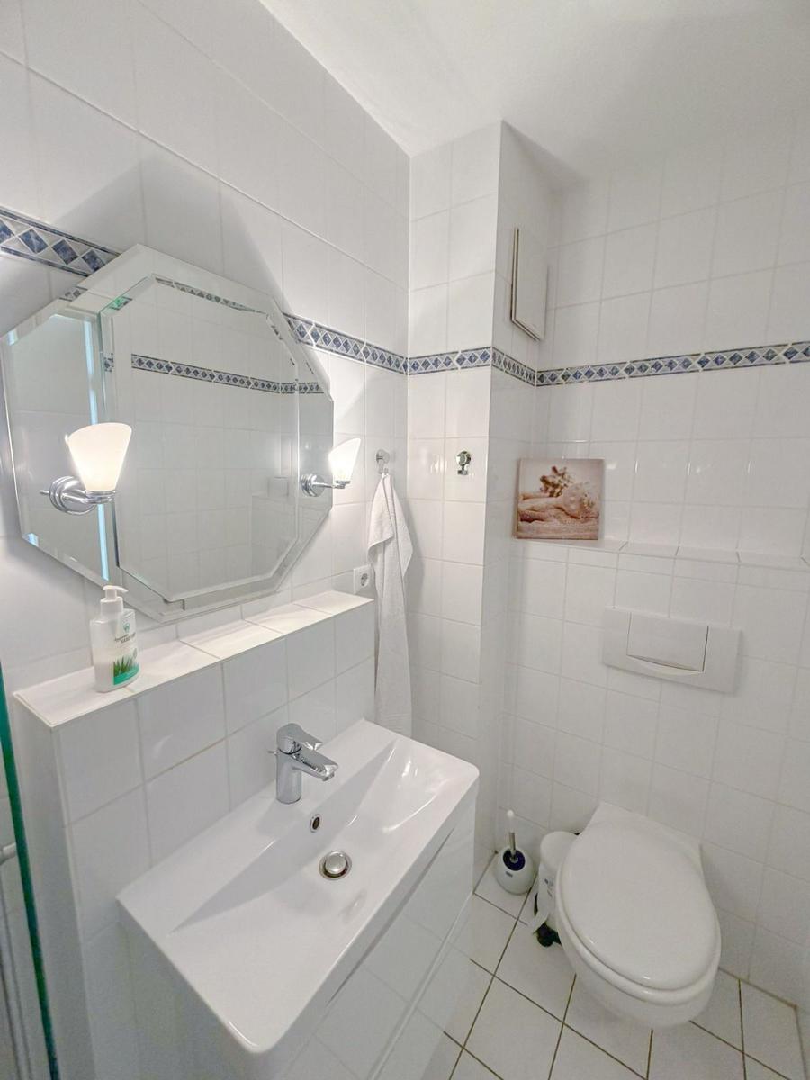 Bathroom with sink, mirror, and toilet. White tiles and blue decorative strip.